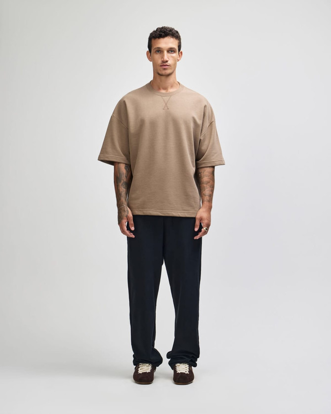 A model wearing a brown oversized boxy top paired with dark pants, standing against a neutral background.