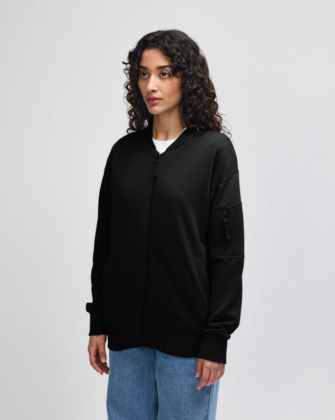 A black unisex bomber jacket with a zippered sleeve pocket, displayed on a model from the side.