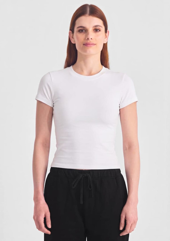 A white women's baby tee with short sleeves, paired with black pants, displayed against a plain background.