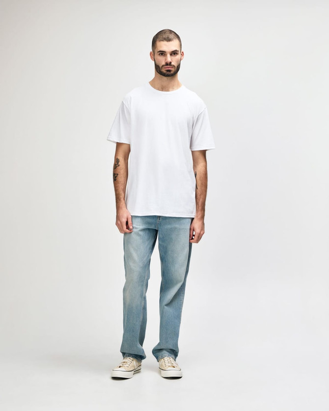 A model wears a white midweight T-shirt paired with black jeans and sneakers, featuring a logo on the shirt.