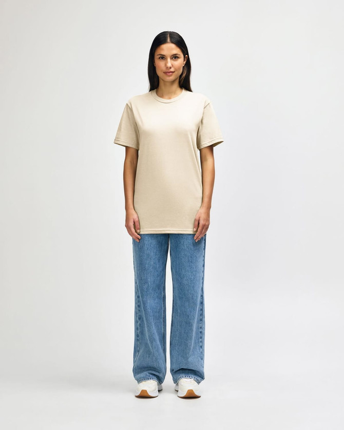 A light khaki midweight t-shirt is worn by a model paired with black pants and sneakers, also featuring a logo.