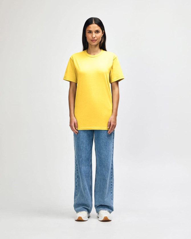 A midweight adult t-shirt in bright yellow, paired with black pants and black sneakers, featuring a logo.