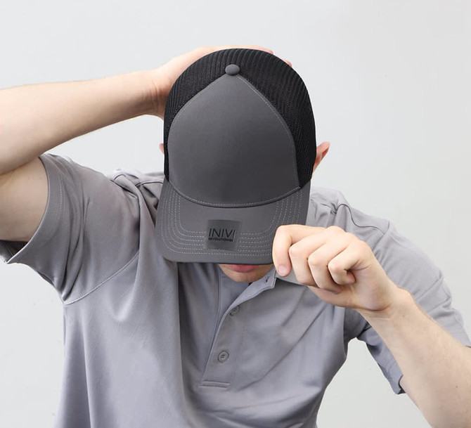 A grey polyester and mesh trucker cap with a branded logo, being worn by a person.