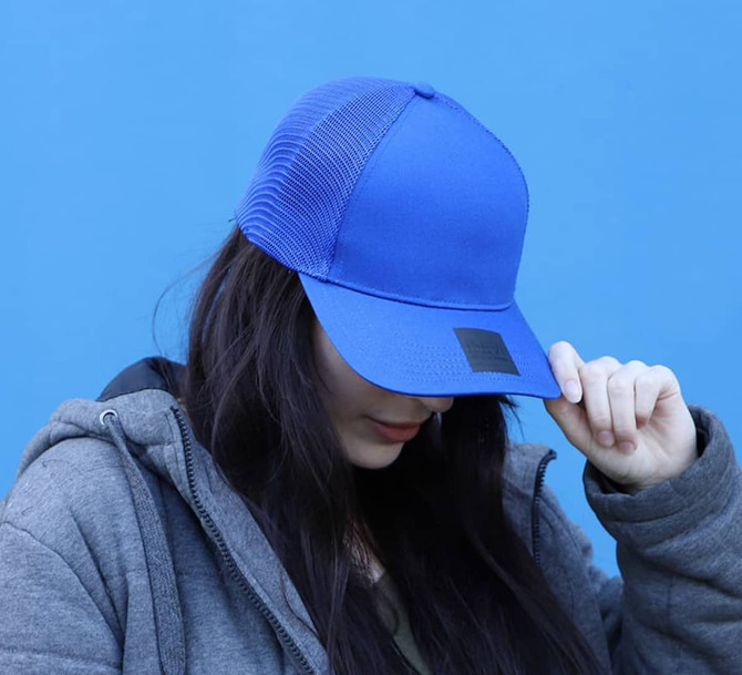 A blue cap with a mesh back and a logo, worn by a person with long dark hair, set against a blue background.