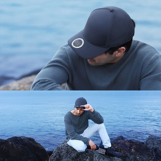 A grey cap with a logo, worn by a man sitting on rocks by the ocean, against a serene water backdrop.