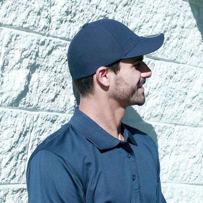 A man in a navy blue cap stands against a textured white wall, wearing a matching navy polo shirt.