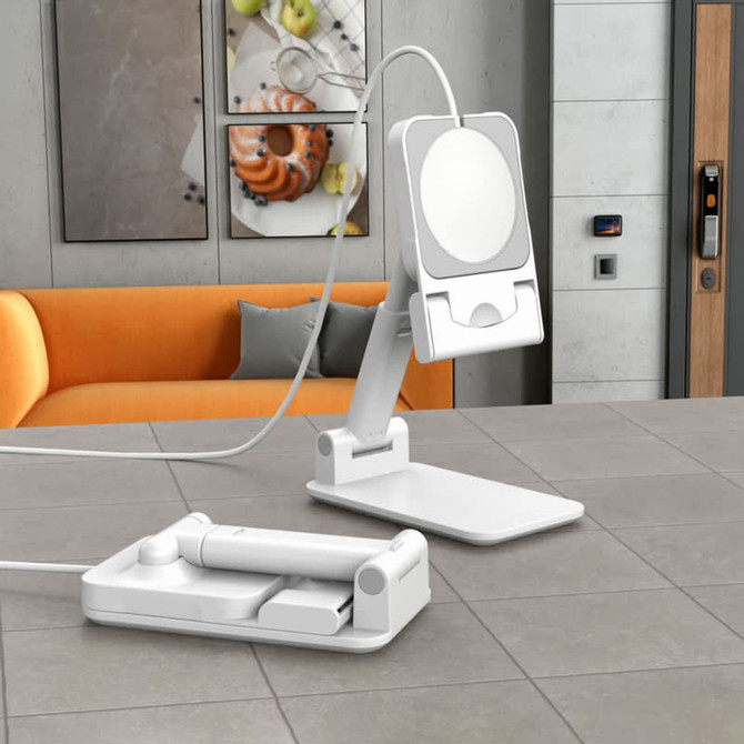 A white magnetic wireless charger with an adjustable stand, placed on a grey countertop beside an orange sofa.