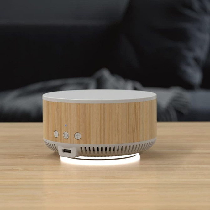 A wireless charging speaker with a bamboo design and white accents, featuring buttons and a branding logo.