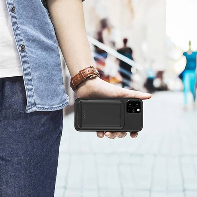 A black magnetic wireless power bank is attached to a smartphone held in a person's hand, with a blurred background.