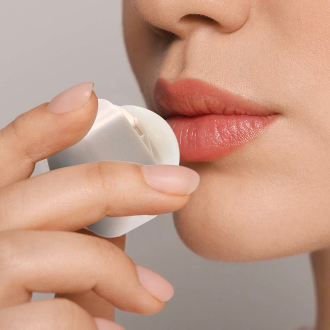 A person applying Ritz Cube Lip Balm to their lips, showcasing the product's sleek packaging and natural lip color.