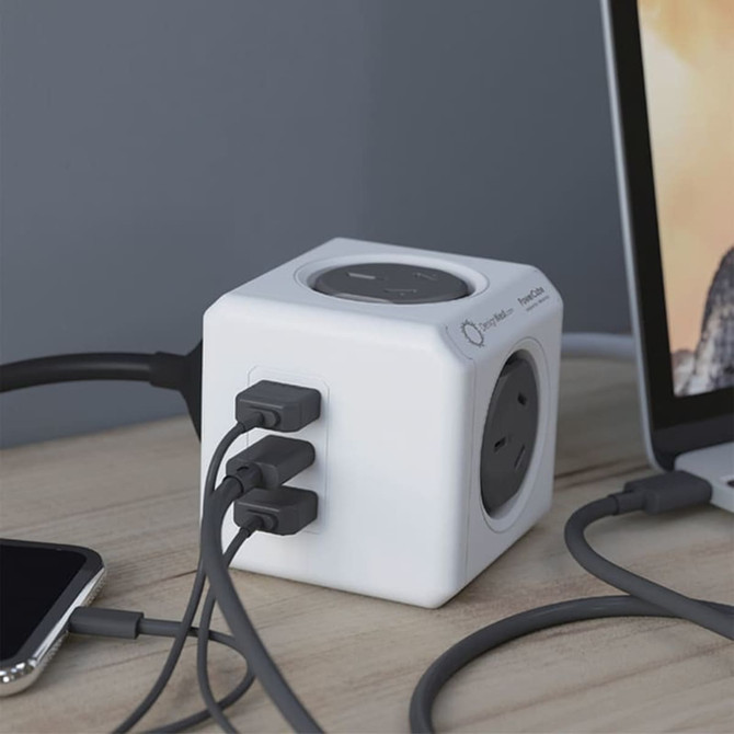 A white power cube with three USB ports and one socket, connected to devices on a wooden surface.