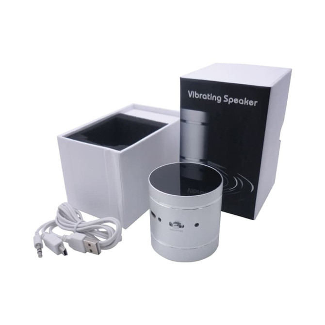 A silver vibrating speaker with a glossy top, accompanied by a USB cable and packaged in a white box.
