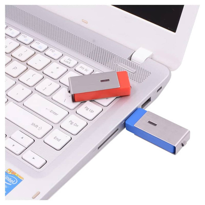 A red and blue Ginan Swivel Flash Drive plugged into a laptop USB port, positioned on a silver laptop keyboard.