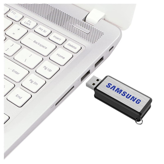 A black and silver flash drive is connected to a laptop's USB port, featuring a logo.