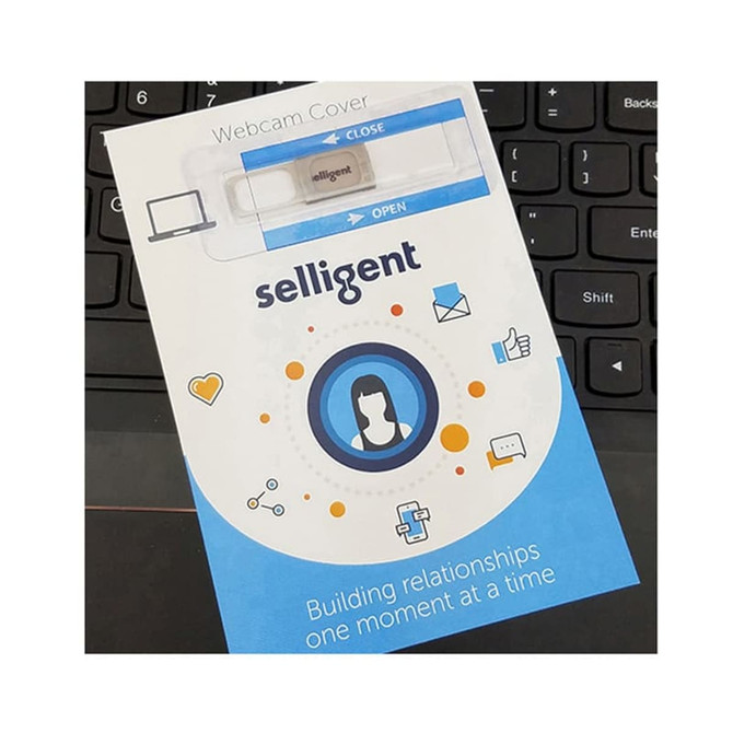 A webcam cover in a white and blue packaging, with a logo, placed on a black keyboard.