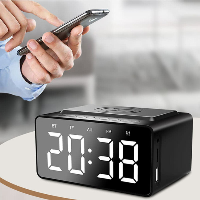 A black alarm clock with a wireless charging area and large digital display, placed on a table.