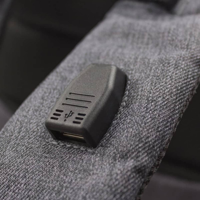 A grey backpack strap featuring a USB port. The fabric has a textured appearance.