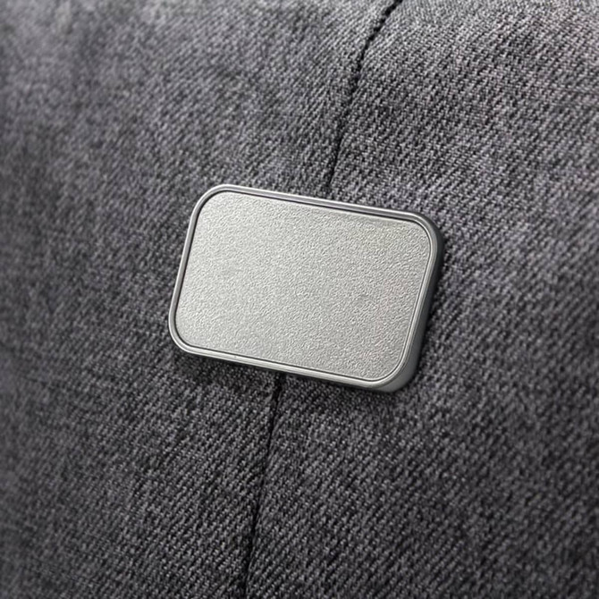 A grey fabric backpack features a textured, rectangular badge on its side, which is likely a logo or branding.