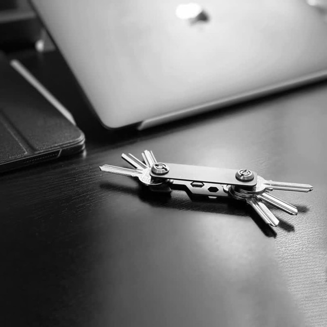 A silver multi-tool keyring with various metal keys laid on a dark wooden surface next to electronic devices.