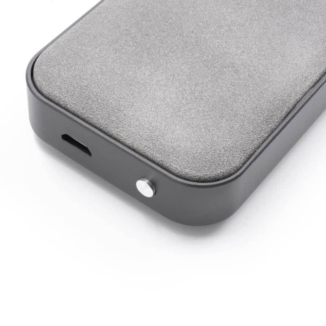 A grey wireless speaker with a smooth surface, featuring a port and a button. It has a minimalist design with a logo.