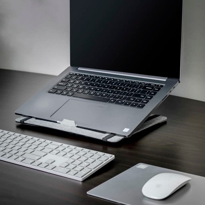 A grey laptop stand with a laptop, white keyboard, and mouse on a dark wooden desk.