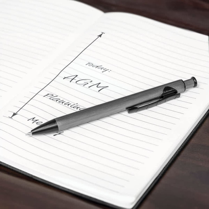 A metal pen with a sleek grey finish rests on a lined notebook, which features handwritten notes.