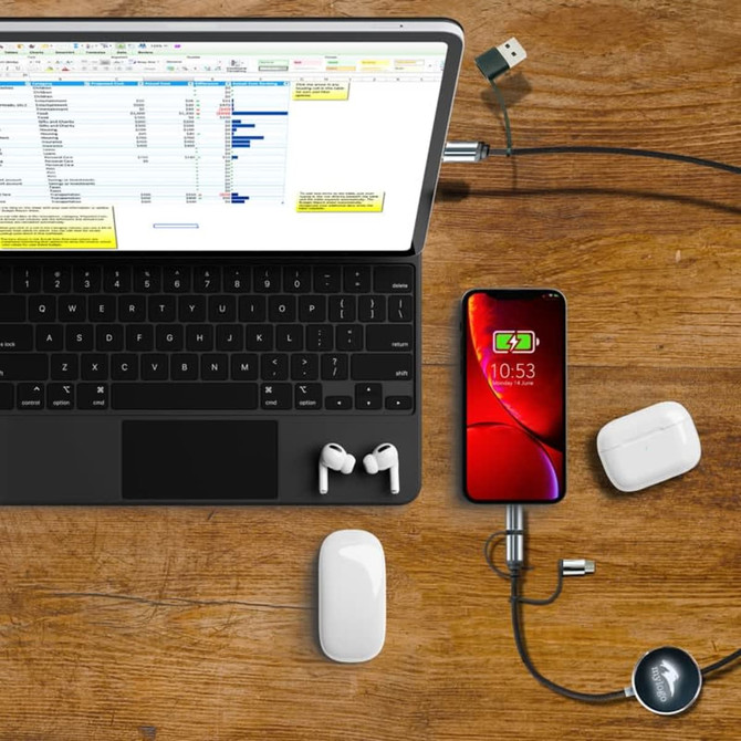 A charging cable with a sleek design connects a smartphone to a laptop, accompanied by wireless earbuds on a wooden surface.