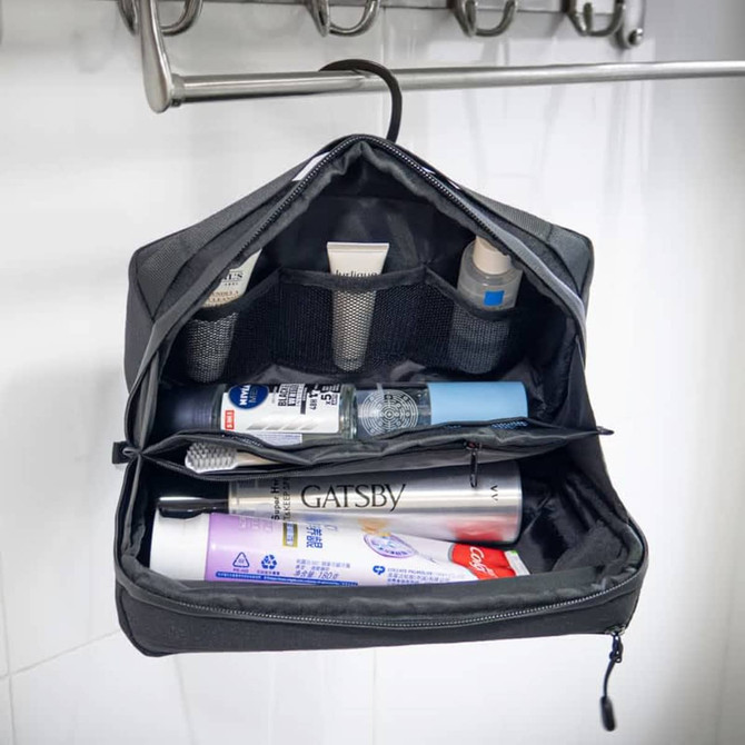 A black toiletry bag hanging open, featuring compartments with various travel-sized toiletries and a logo inside.