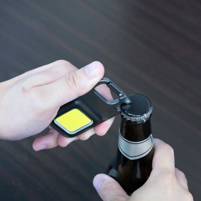 A multi-tool bottle opener with a black body and yellow grip, being used to open a bottle.