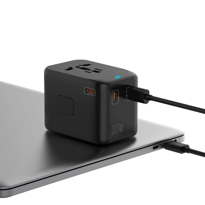 A compact black travel adaptor with multiple ports sits on a laptop, featuring a logo and connected cables.