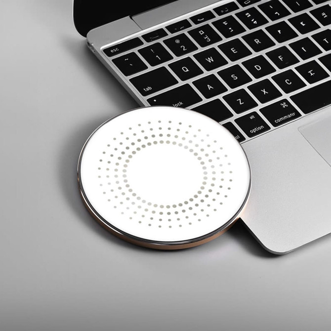 A round, white wireless charger with a dotted pattern, placed next to a laptop keyboard. The charger has a metallic edge.