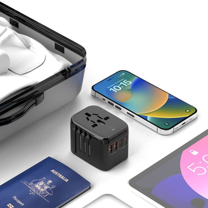 A black travel adaptor with multiple ports, placed beside a smartphone, passport, and a clear case on a flat surface.