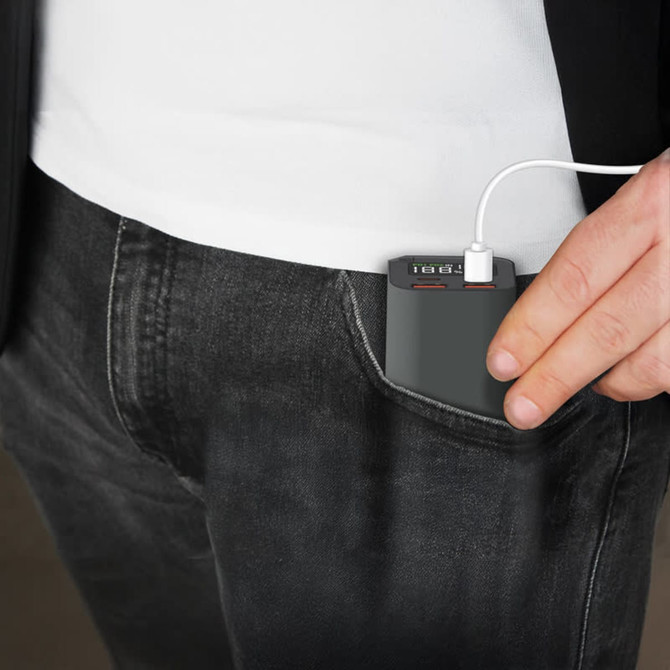 A compact grey power bank with USB ports is being pulled from a pocket, connected to a charging cable.