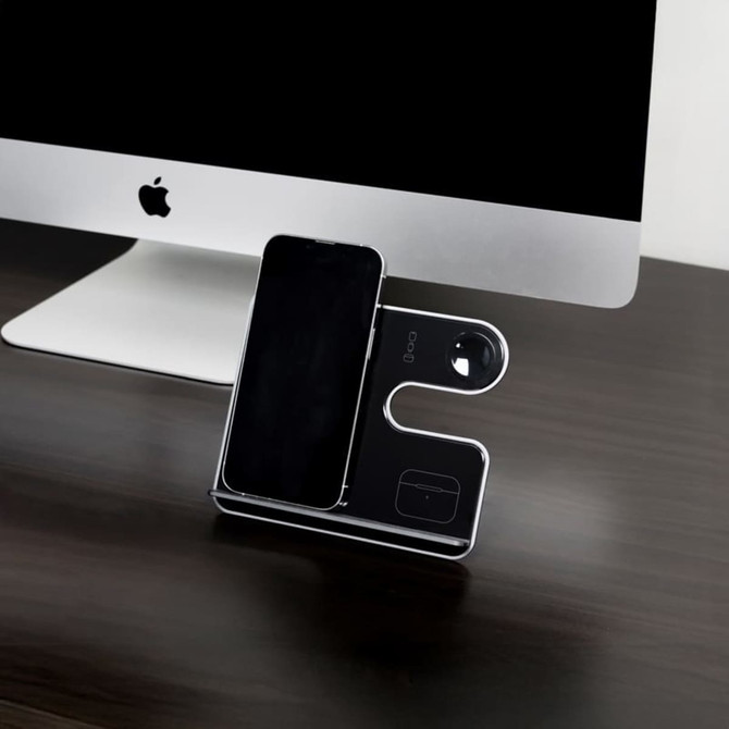 A sleek black and silver wireless charging stand for a phone and other devices, positioned next to a computer.