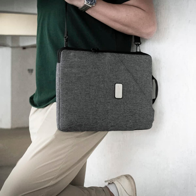 A grey laptop sling bag with a handle and adjustable strap worn by a person. The bag features a logo.