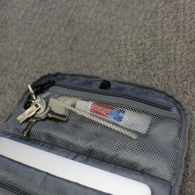A grey backpack pocket containing keys, a white tube, and a pen, all secured in a mesh compartment.
