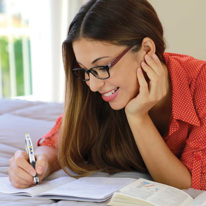 A woman with long hair and glasses is writing with a black and white stylus pen on an open book.