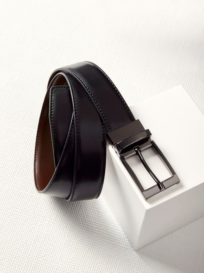 A reversible men's leather belt featuring a sleek black finish and a metal buckle, displayed on a white surface.