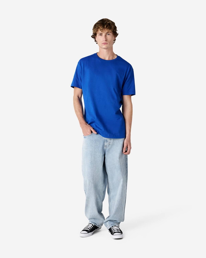 A blue heavyweight cotton unisex T-shirt is worn by a person paired with light blue jeans and black sneakers.