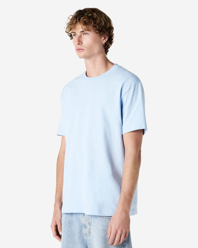 A light blue heavyweight cotton unisex t-shirt on a model, featuring a simple design and a logo.