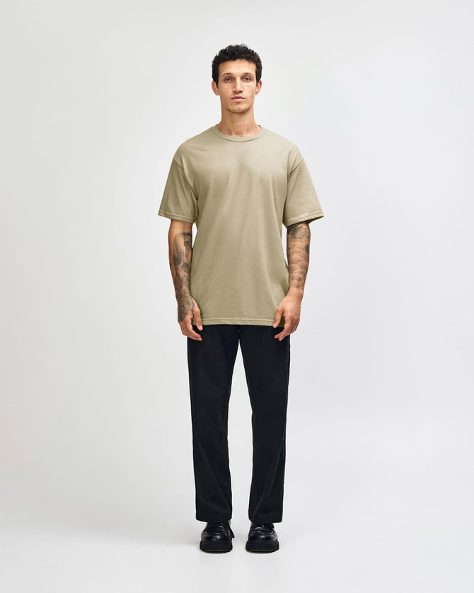 A unisex heavyweight cotton t-shirt in olive green, paired with light blue cargo jeans. The model has curly hair.