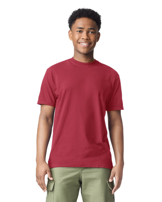 A red adult heavyweight t-shirt displayed on a smiling young model wearing olive green pants. The shirt features a logo.
