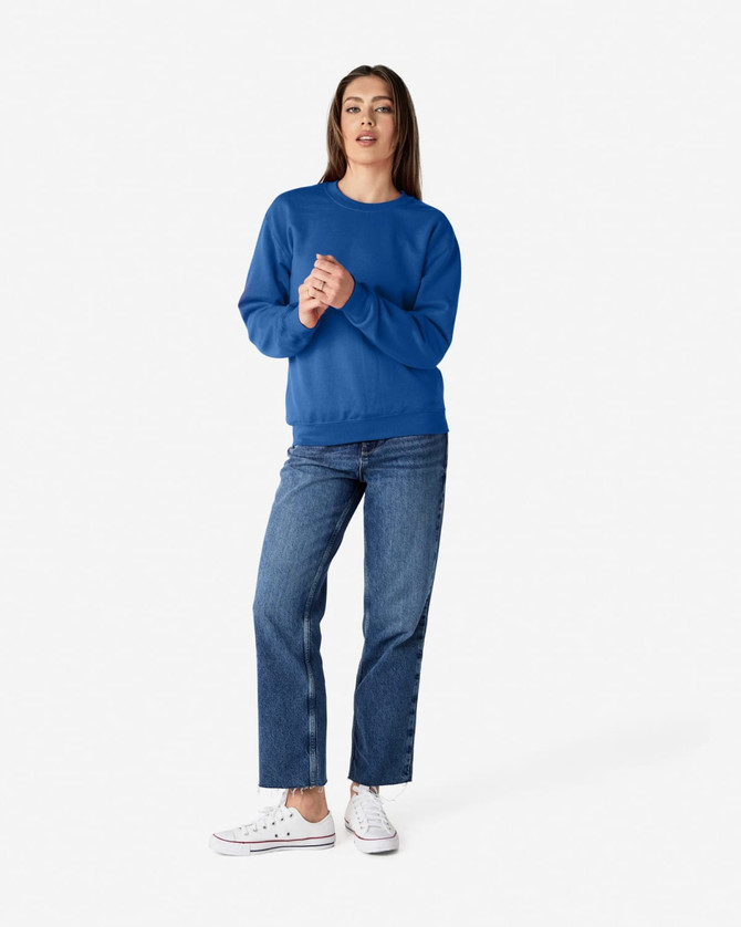 A woman wearing a blue Gildan Heavy Blend crewneck sweatshirt paired with blue jeans and white sneakers.