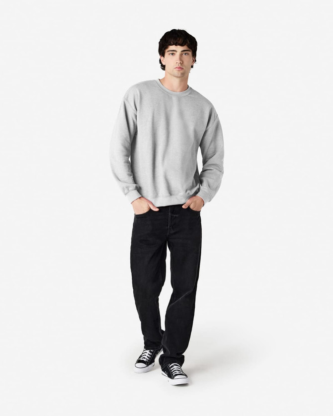 A grey Gildan Heavy Blend adult crewneck sweatshirt worn by a model, paired with black jeans and sneakers.