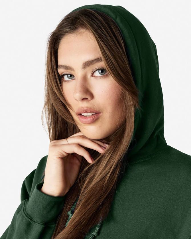 A green hooded sweatshirt worn by a woman with long hair, featuring a hood and a logo.