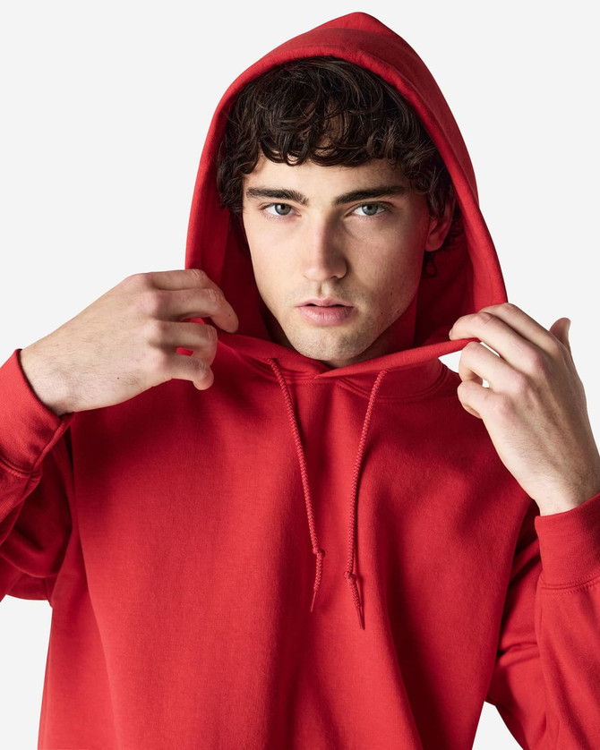 A red Gildan Heavy Blend adult hooded sweatshirt worn by a model, featuring a hood and drawstrings.