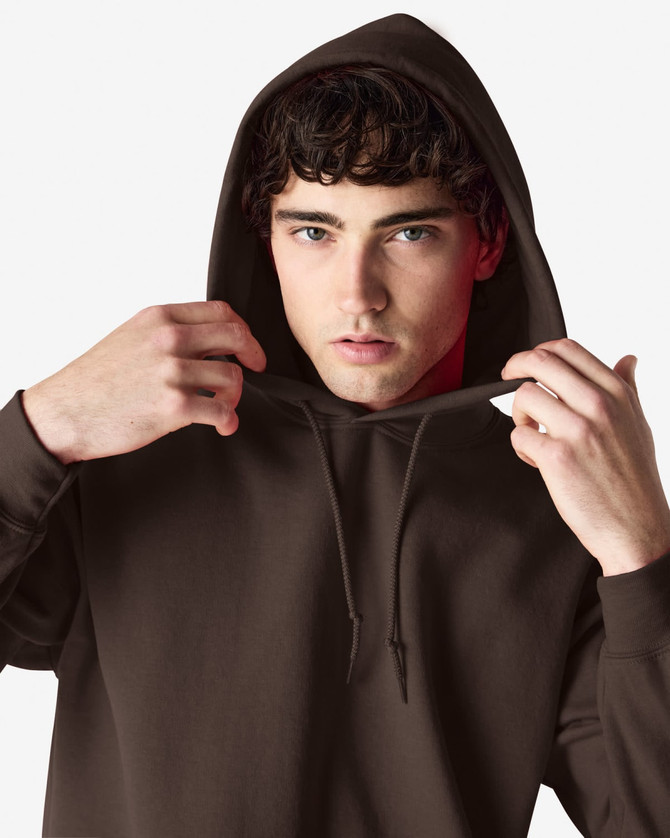 A brown hooded sweatshirt featuring a drawstring hood and a model adjusting it. The design has a logo.