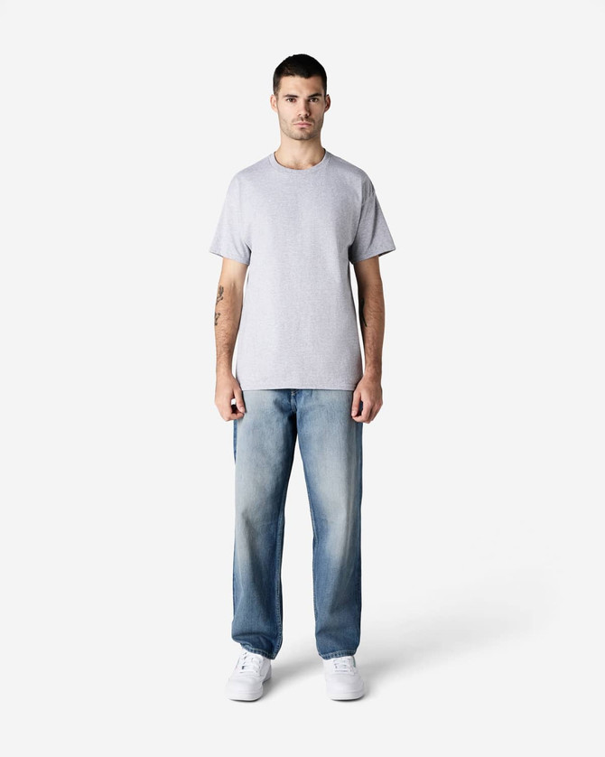 A man stands wearing a light grey Gildan Ultra Cotton Adult T-Shirt and blue jeans, with white sneakers.