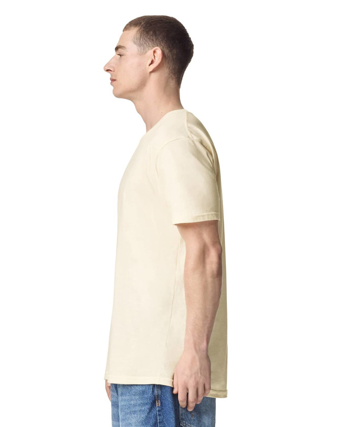 A side view of a beige unisex short sleeve t-shirt worn by a model, featuring a logo on the sleeve.