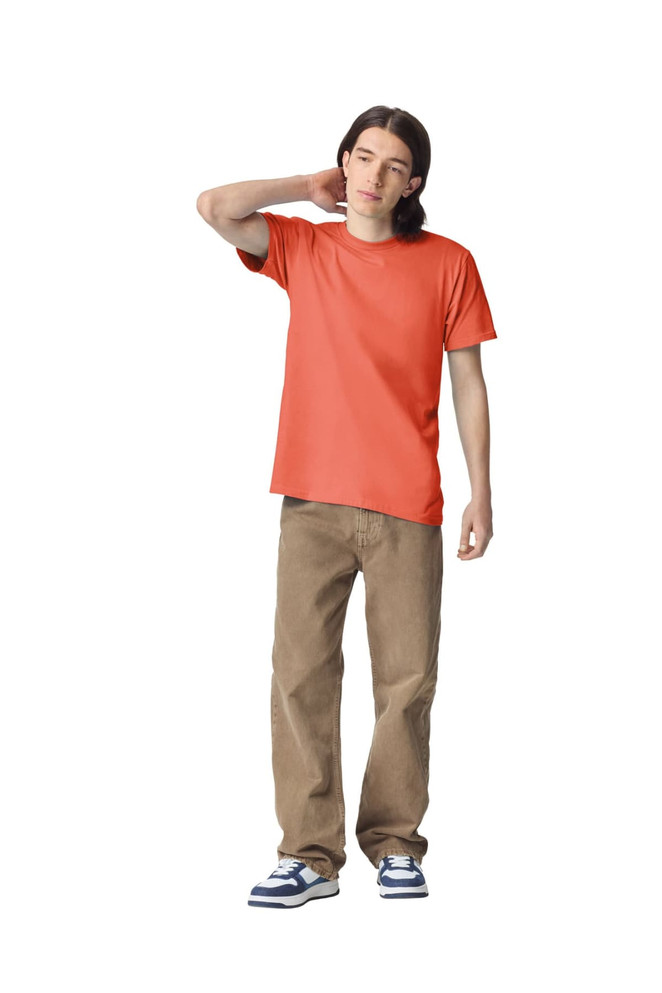 A model wearing an orange unisex short sleeve t-shirt and beige pants, standing casually. The t-shirt has a logo.